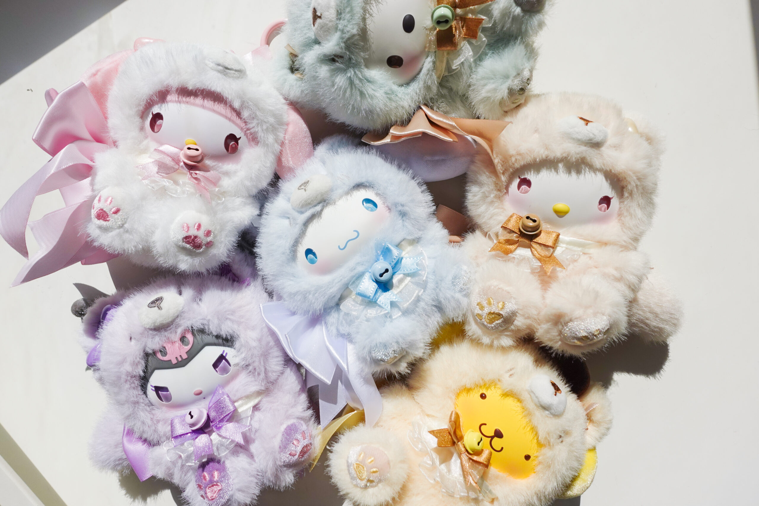 Collection of pastel Sanrio character plush toys wearing fluffy animal-style hooded outfits in pink, blue, cream, green, and purple.