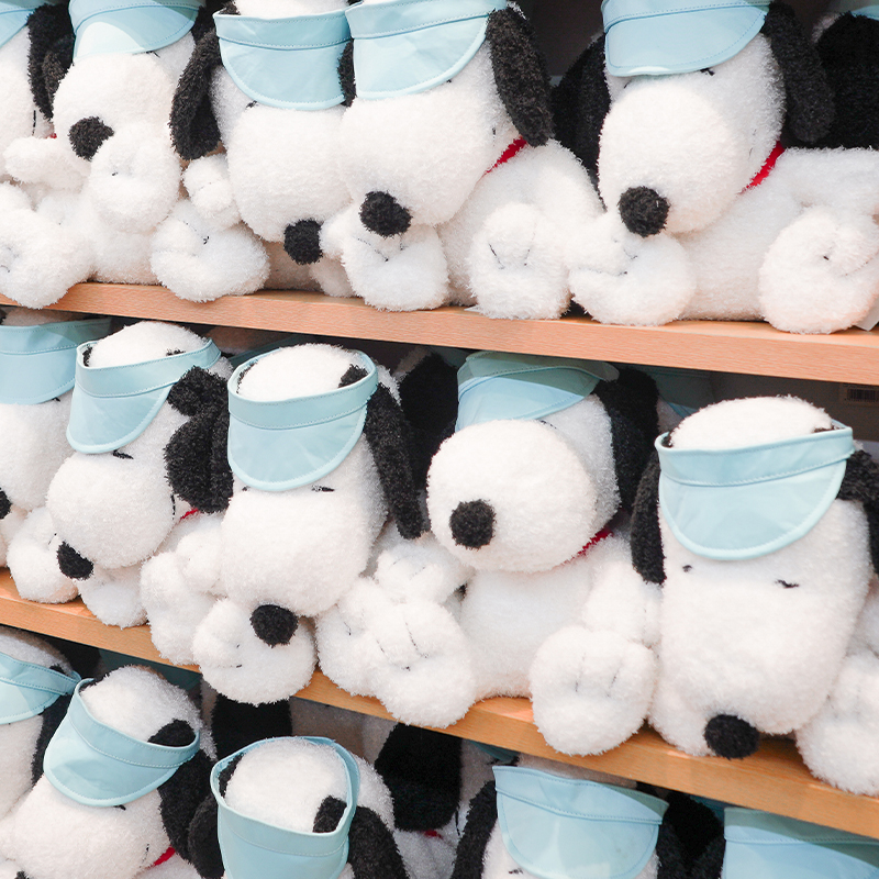 Shelves filled with Snoopy plush toys wearing light blue visors.