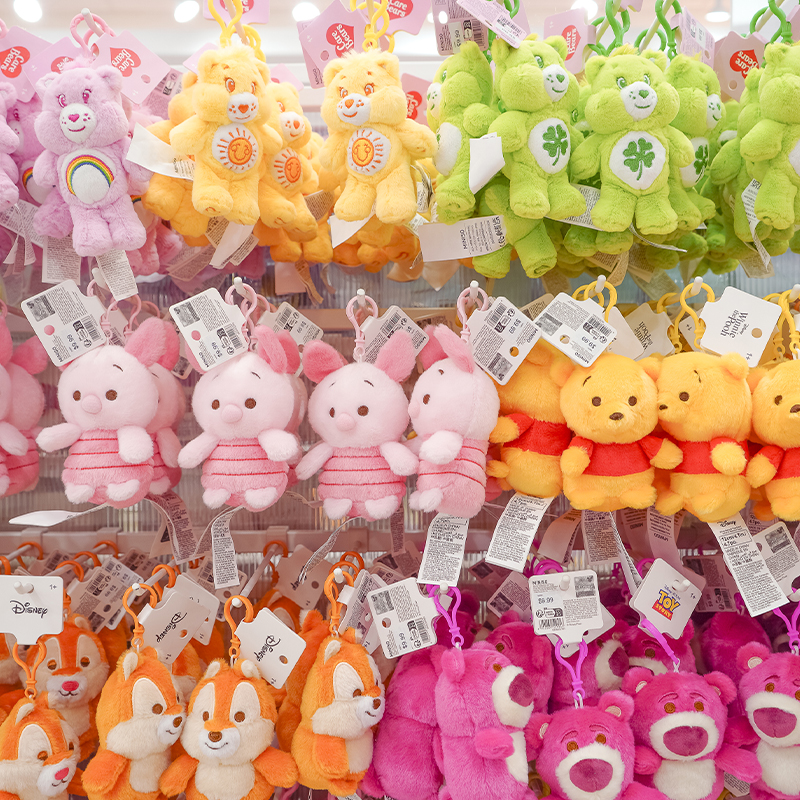 Retail display of colorful plush character keychains including Care Bears, Winnie the Pooh, Piglet, Lotso, and Chip plush toys.