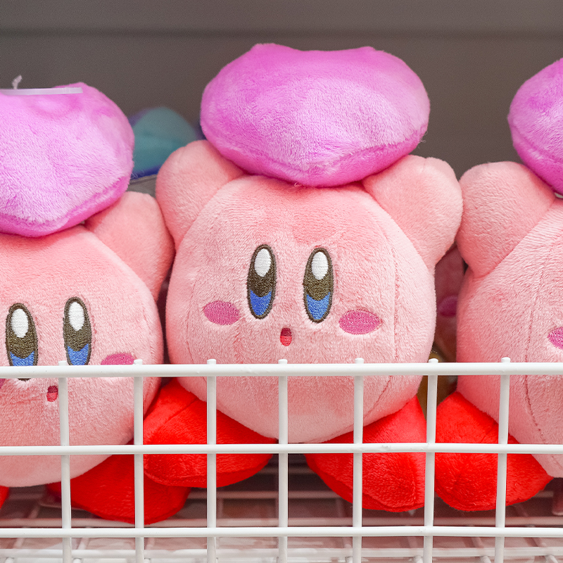 Pink Kirby plush toys with red feet displayed behind a white wire shelf barrier.