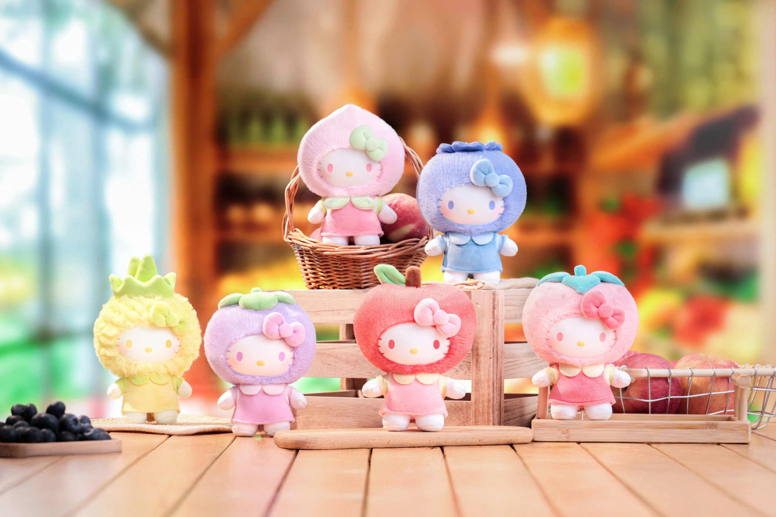 Hello Kitty plush dolls dressed in pastel fruit-inspired outfits displayed on a wooden table with baskets and fruit décor.