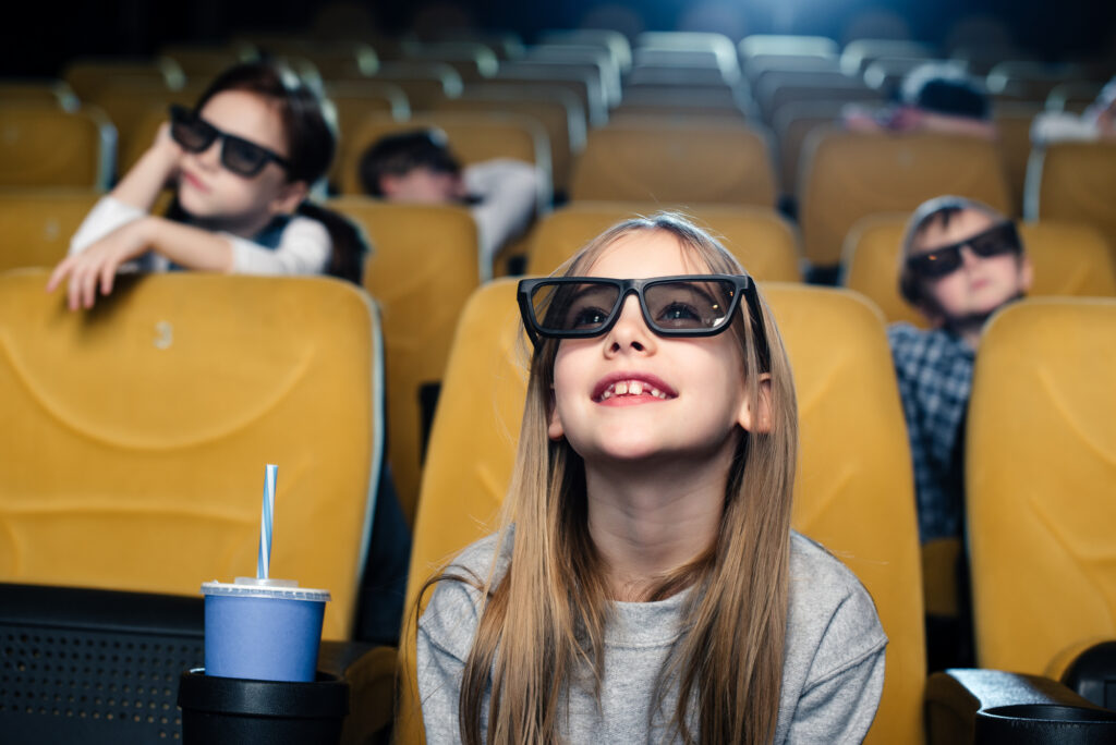 Child wearing 3D glasses watching a movie in a theater with other viewers in the background. Click to view a larger version.